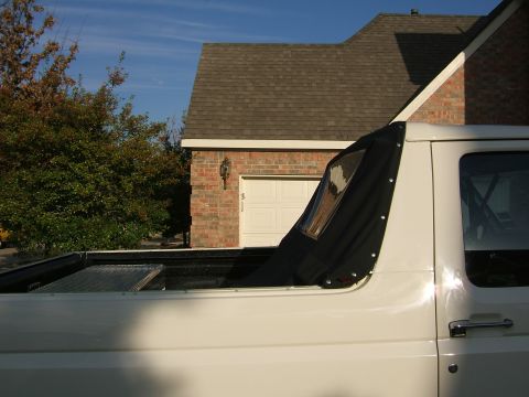 1991 Ford Bronco - Side view of a white Ford truck with its hardtop removed and a black soft top partially unsnapped and folded back behind the cab, exposing…