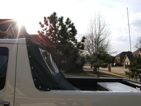 1991 Ford Bronco - A white 1991 Ford Bronco with a black soft top is seen from the side, with a diamond plate toolbox in the bed.