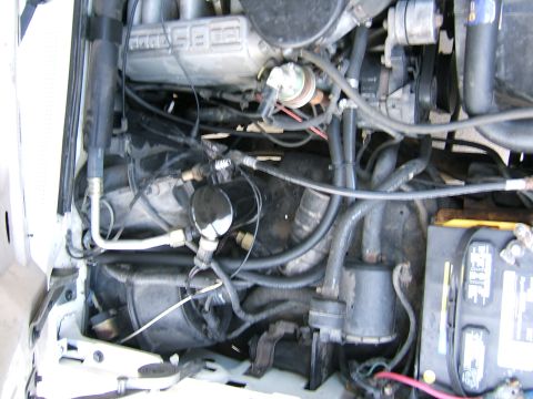 1991 Ford Bronco - Close-up view of a vehicle's engine bay, showing various hoses, wiring, and the battery.