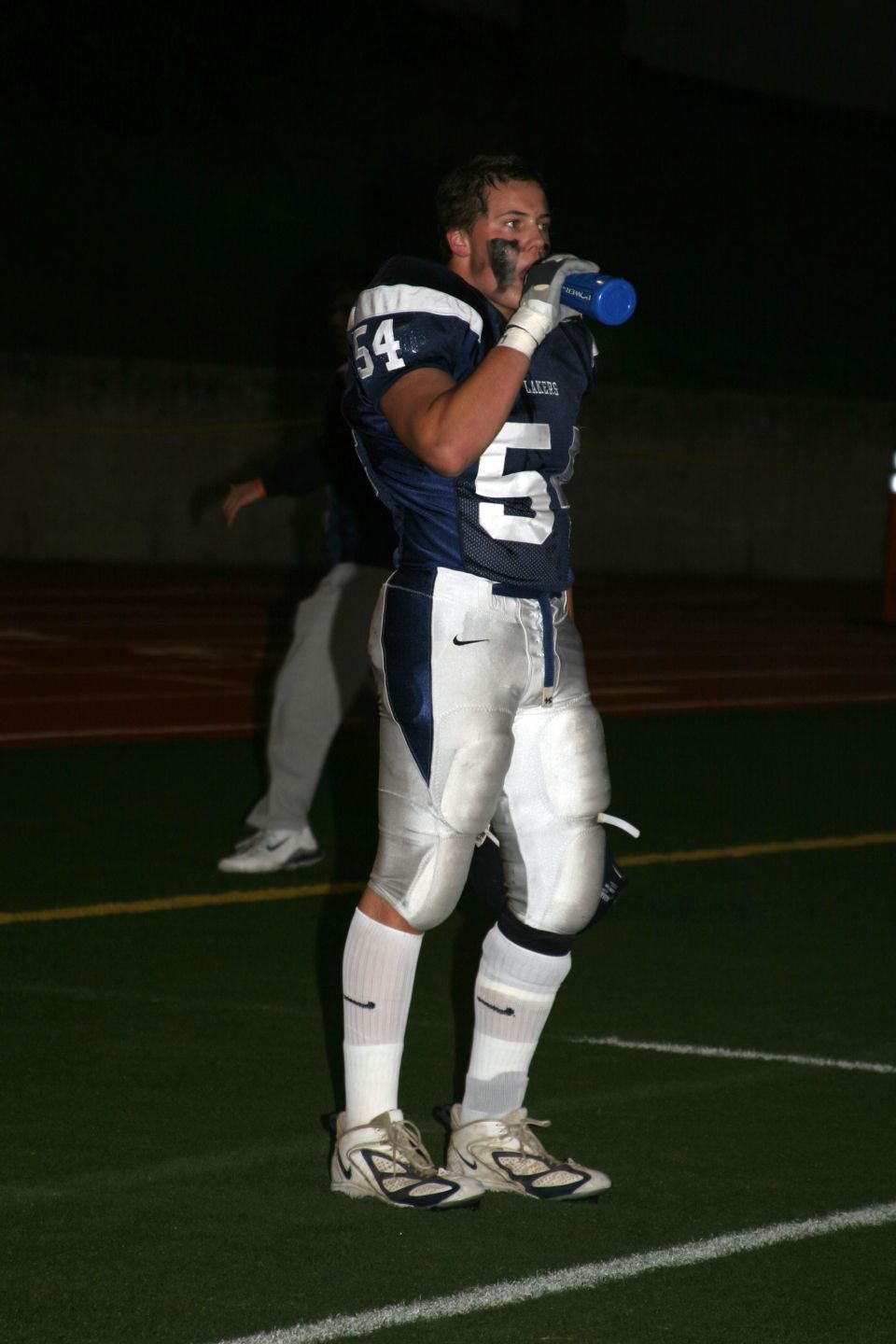 Football player in uniform with number 54 on jersey, drinking from a blue bottle on a green field