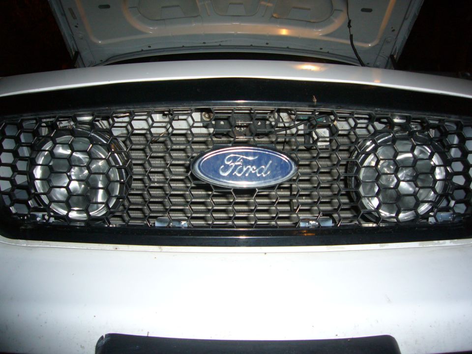 White Ford Crown Victoria front grille with honeycomb pattern and two round fog lights. Ford logo is centered