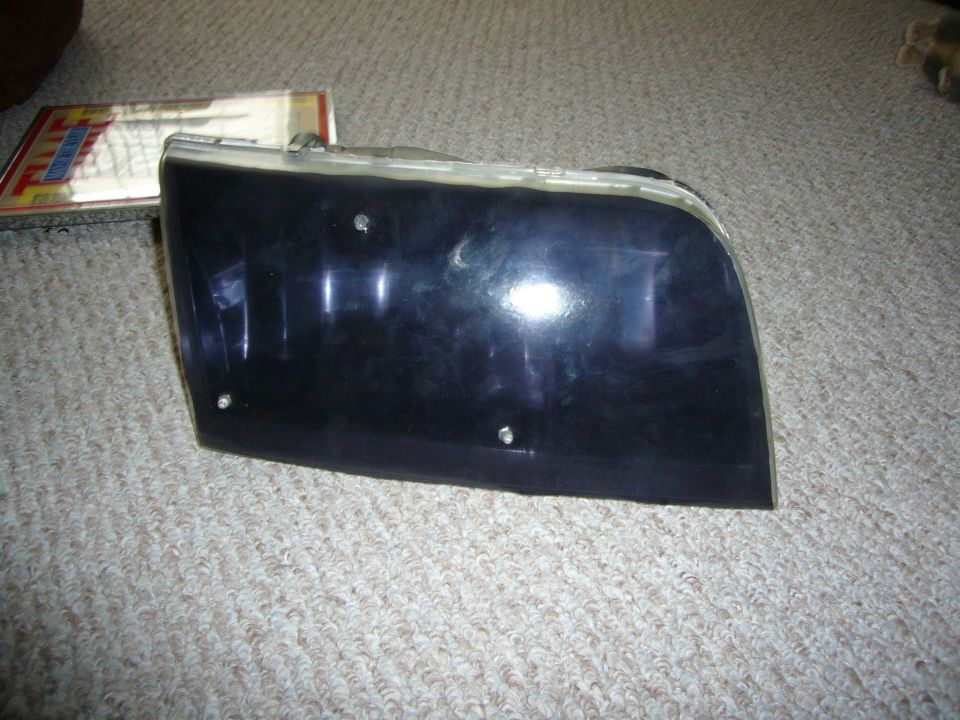 Removed headlight assembly with smoked purple-black tinted lens on carpet