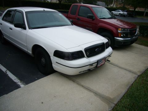 2000 Ford Crown Victoria - A white sedan and a red pickup truck are parked side-by-side on a paved surface.