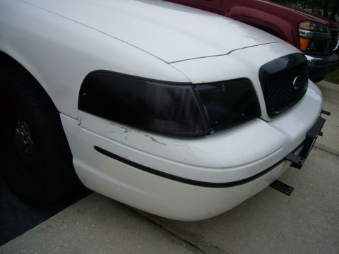 2000 Ford Crown Victoria - The front corner of a white 2000 Ford Crown Victoria is visible, parked next to a red truck.