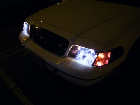 2000 Ford Crown Victoria - The front of a white 2000 Ford Crown Victoria is visible at night, with its headlights illuminated.