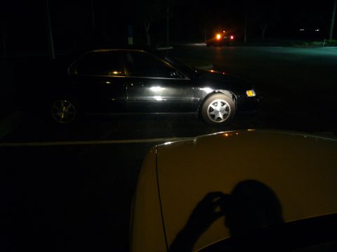 2000 Ford Crown Victoria - A black sedan is parked in a lot at night, with another vehicle partially visible in the foreground.