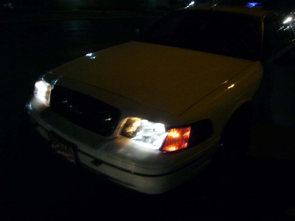 Front view of a white 2000 Ford Crown Victoria with headlights on