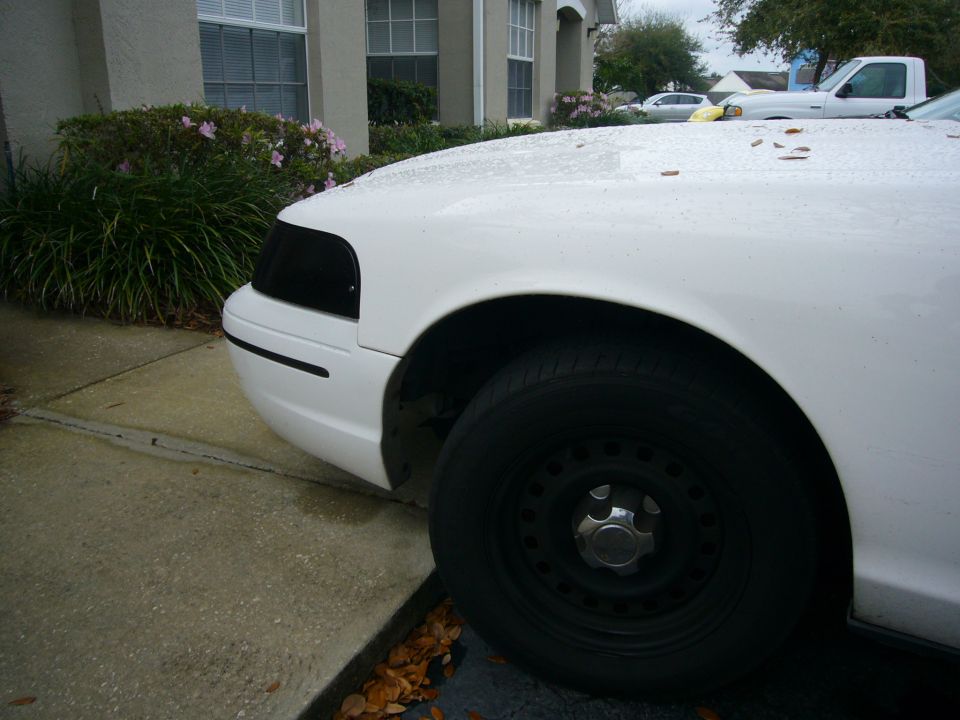 Front corner of a white car with blacked-out headlights and a steel wheel