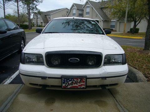 2000 Ford Crown Victoria - Head-on front view of a rain-spotted white Ford full-size sedan parked in an apartment lot, showing smoked headlight lenses, a black mesh g…