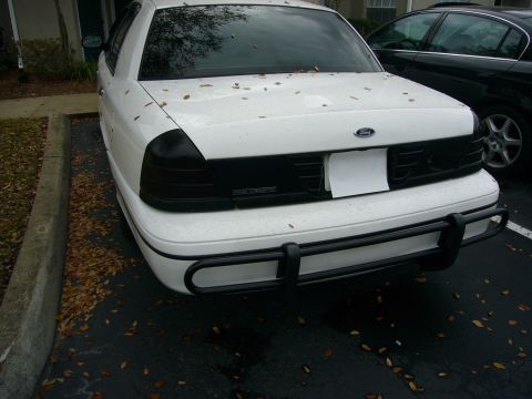 2000 Ford Crown Victoria - Rear three-quarter view of a white Ford Crown Victoria in a leaf-strewn parking lot, wearing smoked/blacked-out tail lights and a black tub…