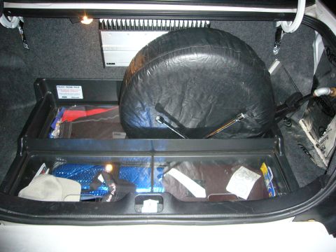 2000 Ford Crown Victoria - Open car trunk showing an upright spare tire and a 'Police Trunk Pack' storage tray holding bags and equipment.