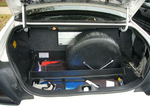 2000 Ford Crown Victoria - Open trunk of a white sedan showing an upright spare tire and a black 'Police Trunk Pack' organizer tray with stored gear.