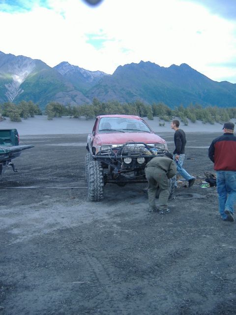 1991 Toyota Tacoma - A modified red pickup truck sits in a dusty, mountainous landscape with several people around it.