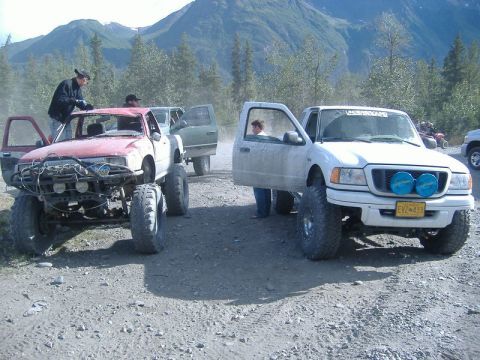 1991 Toyota Tacoma - Modified trucks are parked on a dirt road, with people standing around them and mountains in the distance.