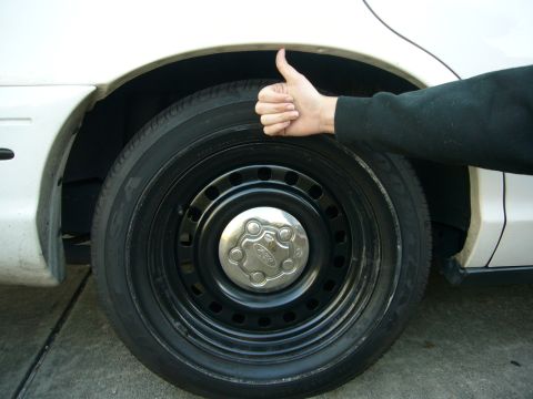 2000 Ford Crown Victoria - A hand gives a thumbs up next to the wheel of a white vehicle, showing the Ford emblem on the hubcap.