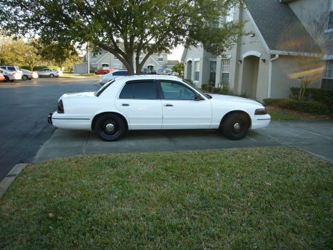 2000 Ford Crown Victoria - A white 2000 Ford Crown Victoria sedan is parked in front of a building with a tree overhead.