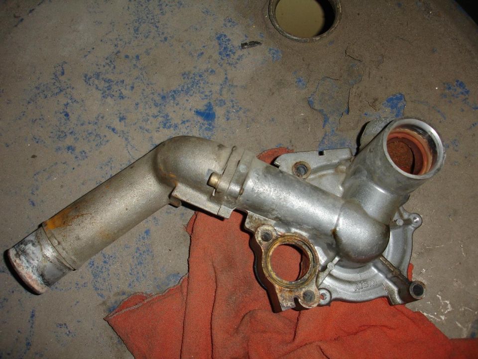 Aluminum Aisin water pump housing with long coolant inlet pipe on a red shop rag