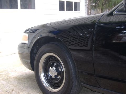2001 Ford Crown Victoria - Close-up of the front passenger side of a black sedan, showing the fender, wheel, and part of the door.