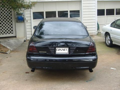 2001 Ford Crown Victoria - The rear of a black sedan is shown parked in a driveway, with a white car to its right.