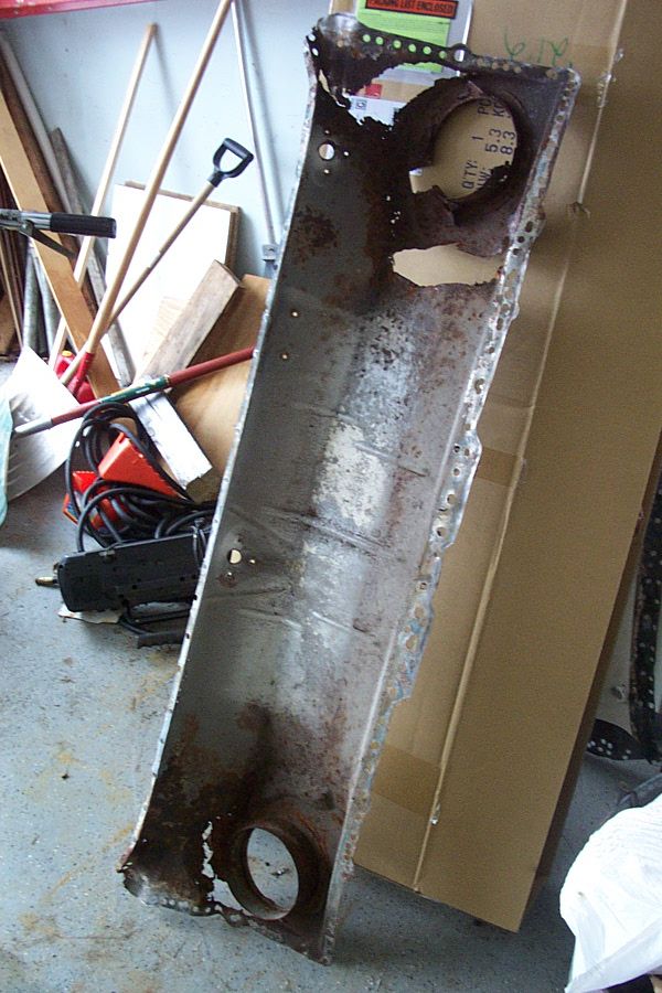 Rusted-out sheet metal cowl panel removed from a car, standing in a garage