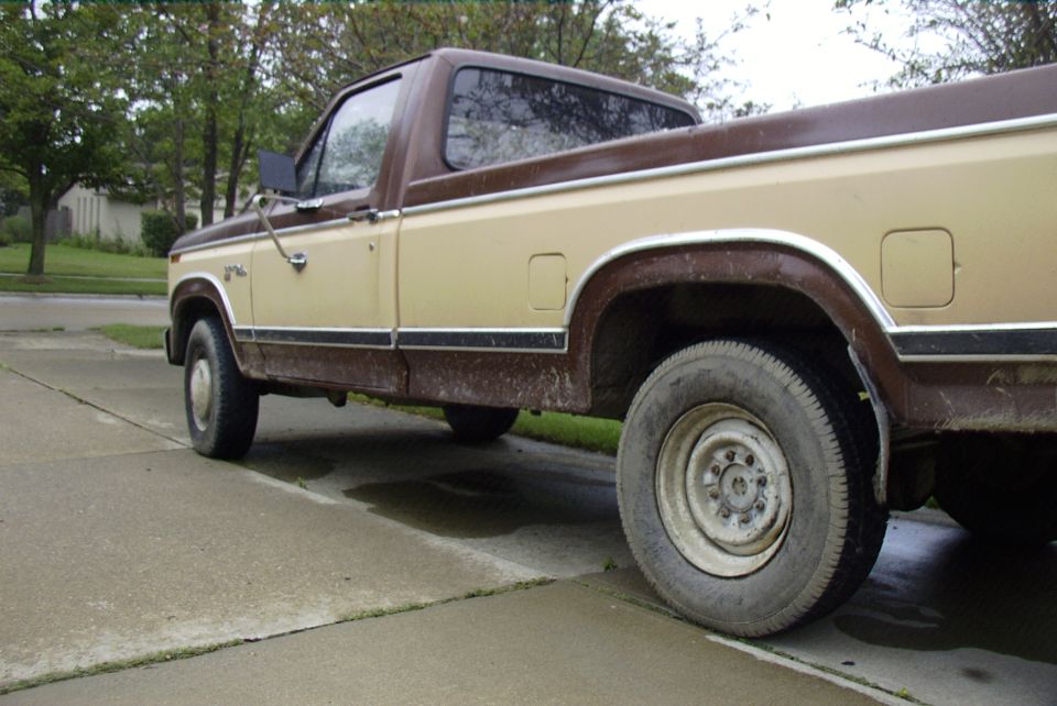 Two-tone brown and tan pickup truck with white steel wheels parked on a wet driveway, side rear view