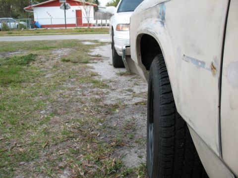 1985 Ford LTD Crown Victoria - Two cars are parked on a dirt lot next to a residential building.