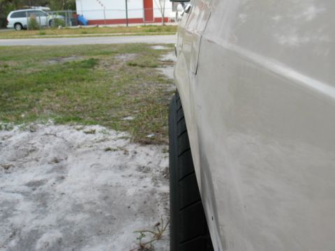 1985 Ford LTD Crown Victoria - Side view of a white car's panel and tire, with another vehicle in the background.