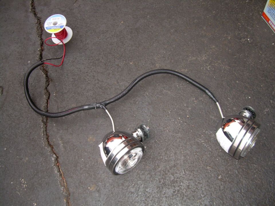 Two chrome trailer lights with wiring harness and spools of wire on a concrete surface