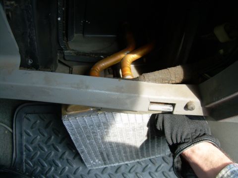 1988 Ford Bronco - A gloved hand removes a heater core from beneath the dashboard, with orange hoses visible in the background.