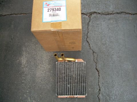 1988 Ford Bronco - A heater core sits on cracked pavement next to a cardboard box with a part number label.