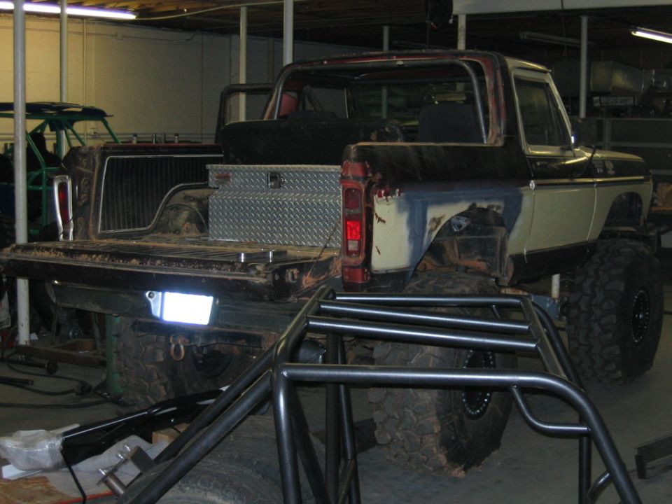 1978 Ford Bronco rear view, lifted with large tires, roll cage in foreground, diamond plate toolbox in bed