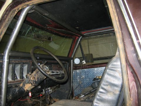1992 Ford Mustang - The interior of a vehicle is visible, a roll cage, a cracked windshield, and diamond plate accents on the door panel.