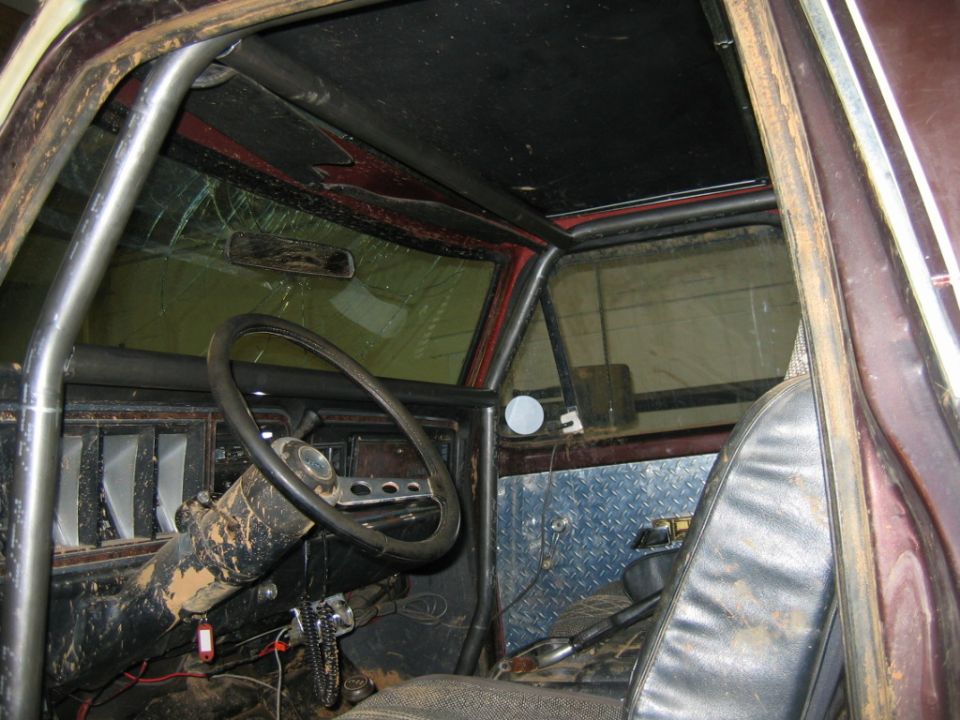 Interior view of a vehicle with a roll cage, cracked windshield, and diamond plate paneling