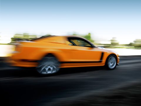 2007 Saleen S-302 - An orange sports car is captured in motion with a blurred background and wheels.