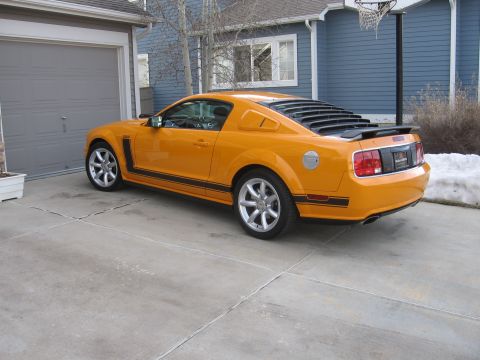2007 Saleen S-302 - A bright orange Ford Mustang is parked in a suburban driveway next to a garage.