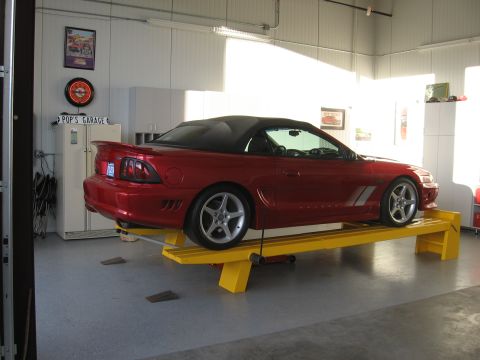 2007 Saleen S-302 - A red convertible Mustang is parked on a yellow lift inside a garage.