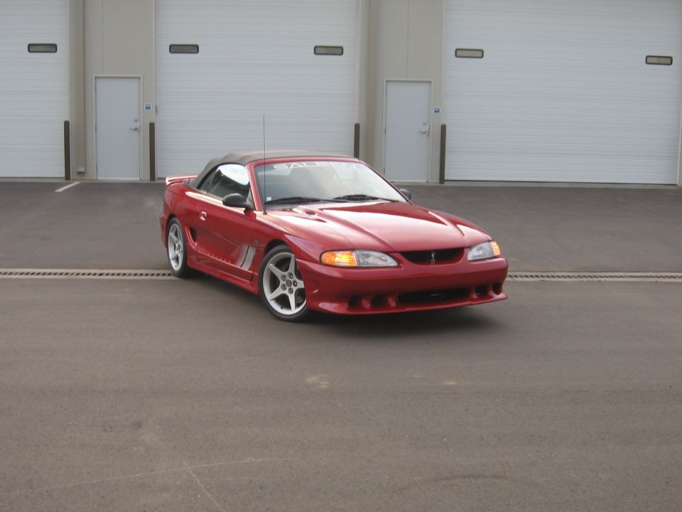Red convertible sports car parked in front of garage doors. Side stripe visible