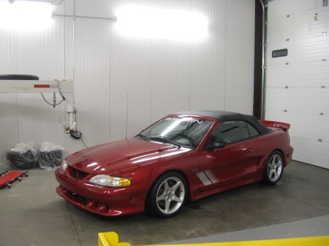 2007 Saleen S-302 - A red convertible Mustang with a black top is parked inside a garage.