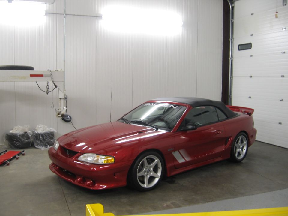 Maroon Mustang convertible with Saleen body kit and silver wheels in a white garage
