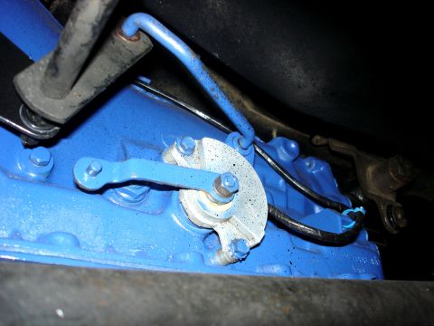 1979 Ford Bronco - A close-up view of a vehicle's transmission linkage, painted bright blue, with visible bolts and mechanical connections.