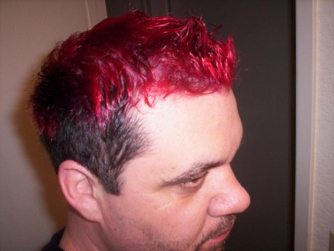 Man with short, spiky, bright red dyed hair and dark stubble, seen in profile