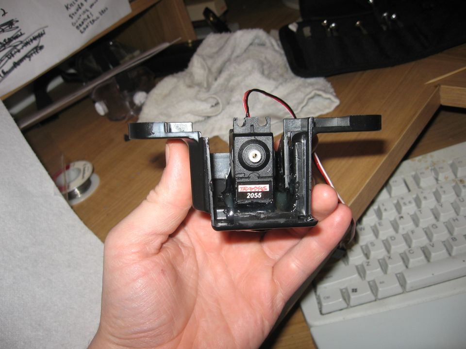 Hand holding black electronic part with red and black wires and a small motor labeled '2055'