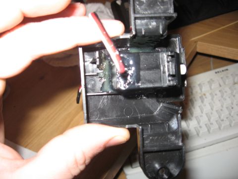 1990 Ford Bronco - A hand holds a small black plastic actuator/servo housing with its cover removed, showing red and black wire leads epoxied into the case wi…