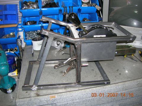 1996 Ford Bronco - A custom-built shifter assembly is clamped to a metal frame, with various parts and bins in the background.