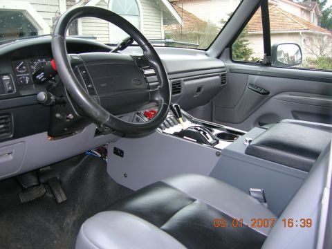1996 Ford Bronco - The interior of a vehicle is shown, the dashboard, steering wheel, and center console.