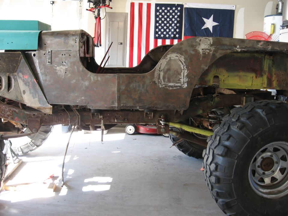 Rusty Jeep CJ-5 body and frame with large tires, undergoing restoration