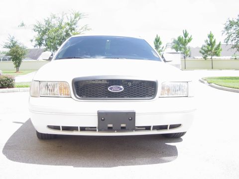 2000 Ford Crown Victoria - The front of a white Ford Crown Victoria is shown, its grille and headlights under a bright sky.