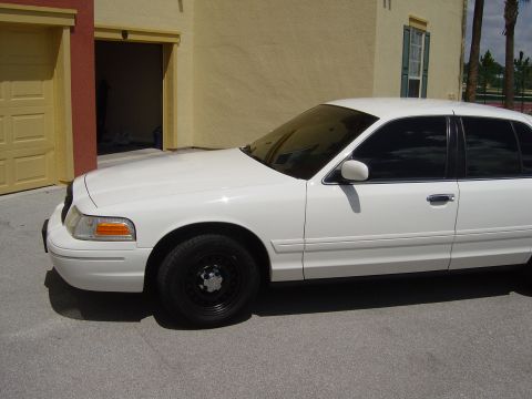 2000 Ford Crown Victoria - A white 2000 Ford Crown Victoria sedan is parked on asphalt in front of a building with a garage.