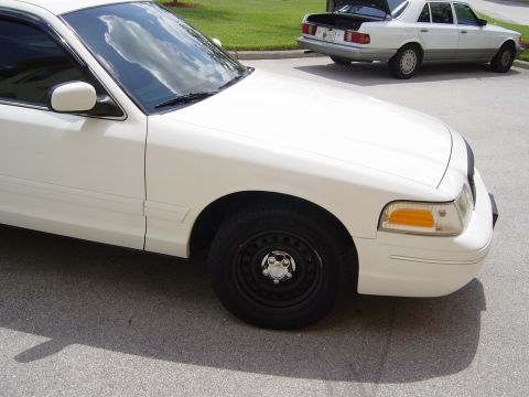 2000 Ford Crown Victoria - A white 2000 Ford Crown Victoria is shown from the front three-quarter view, with another white sedan parked behind it.