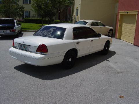 2000 Ford Crown Victoria - A white 2000 Ford Crown Victoria is parked in a driveway next to another car and a garage.